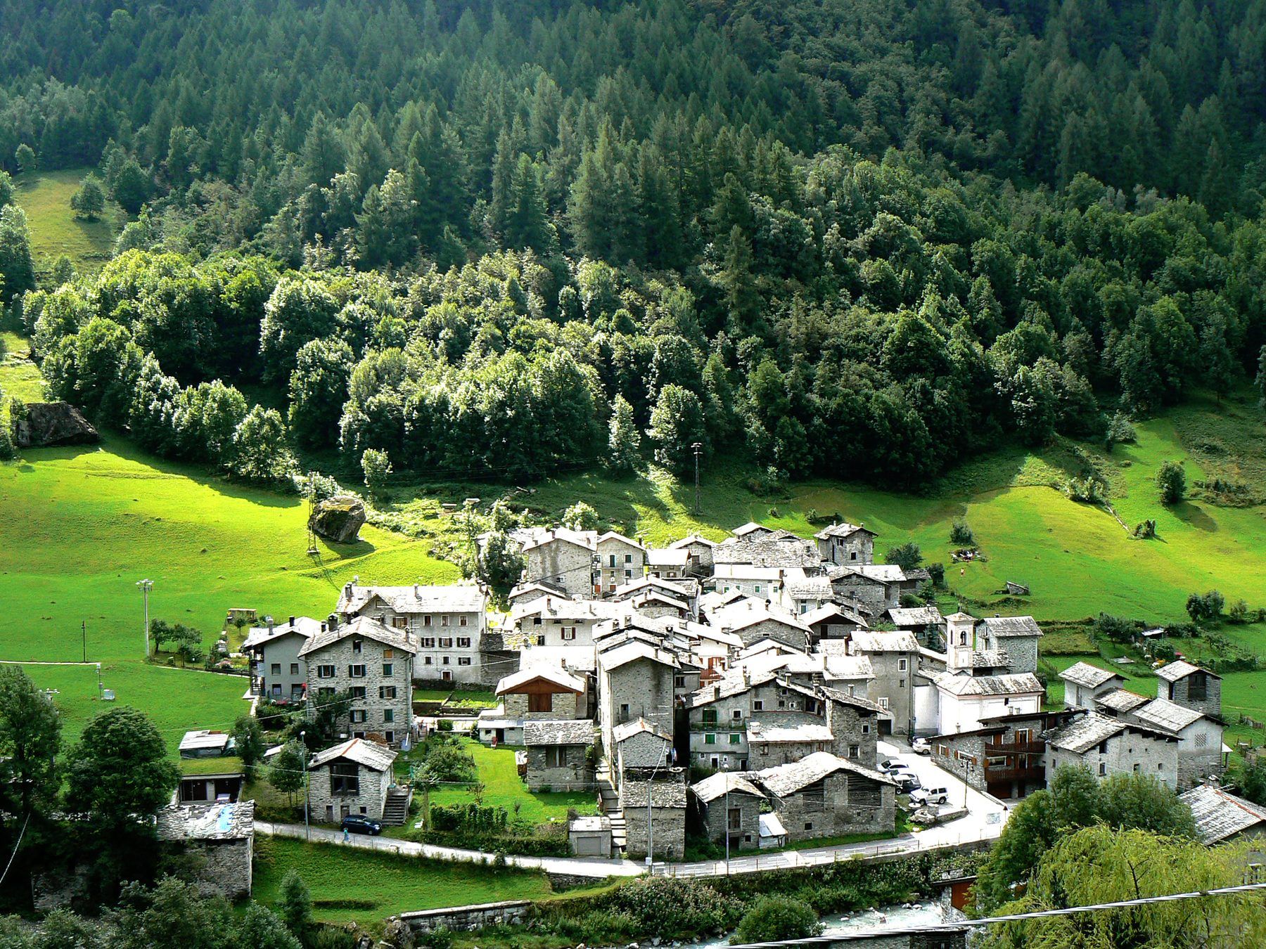 Un paese di montagna con i tetti in pietra, in mezzo a prati verdi e boschi